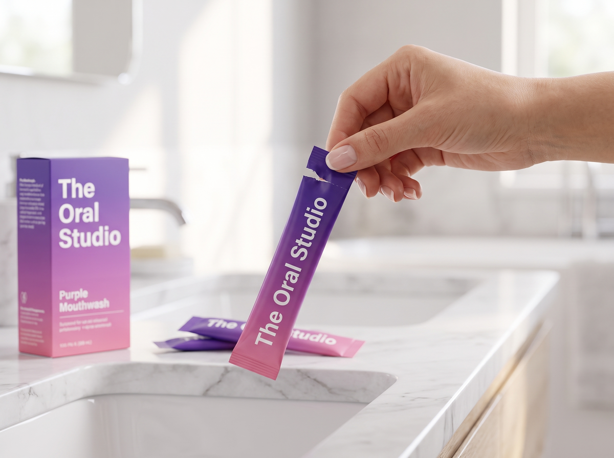 Hand scheurt een sachet Purple Mouthwash open boven een marmeren wastafel